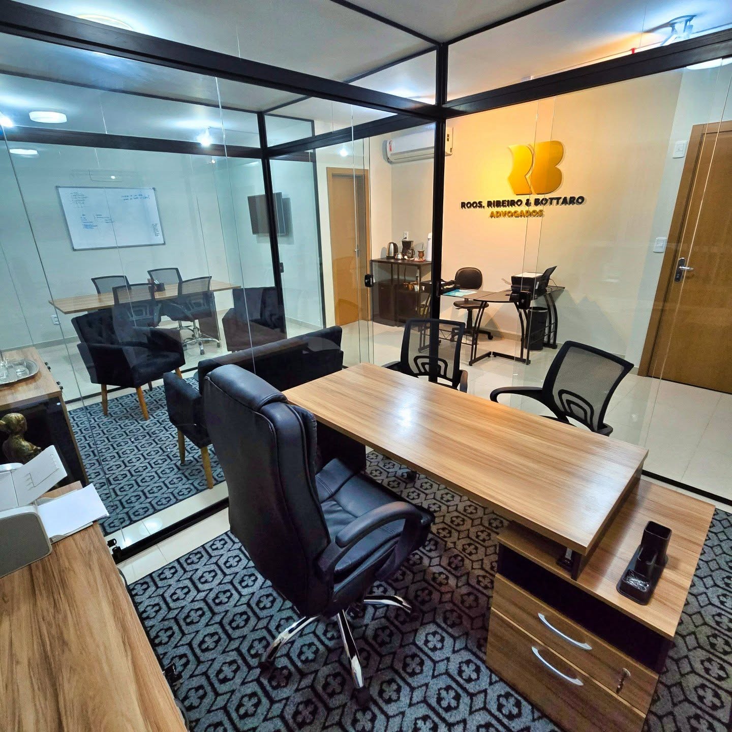 Sala de atendimento do RRB Advogados, com mesa de madeira, cadeiras pretas e a marca RRB dourada na parede