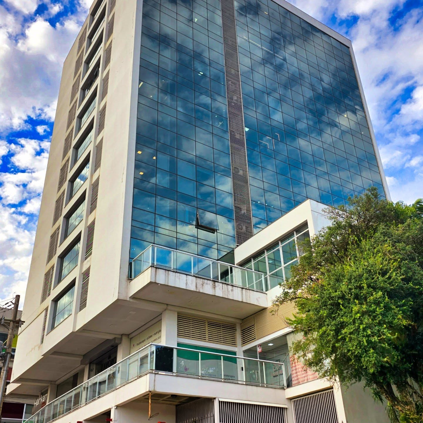 Edifício comercial envidraçado visto de baixo, sob céu azul com nuvens