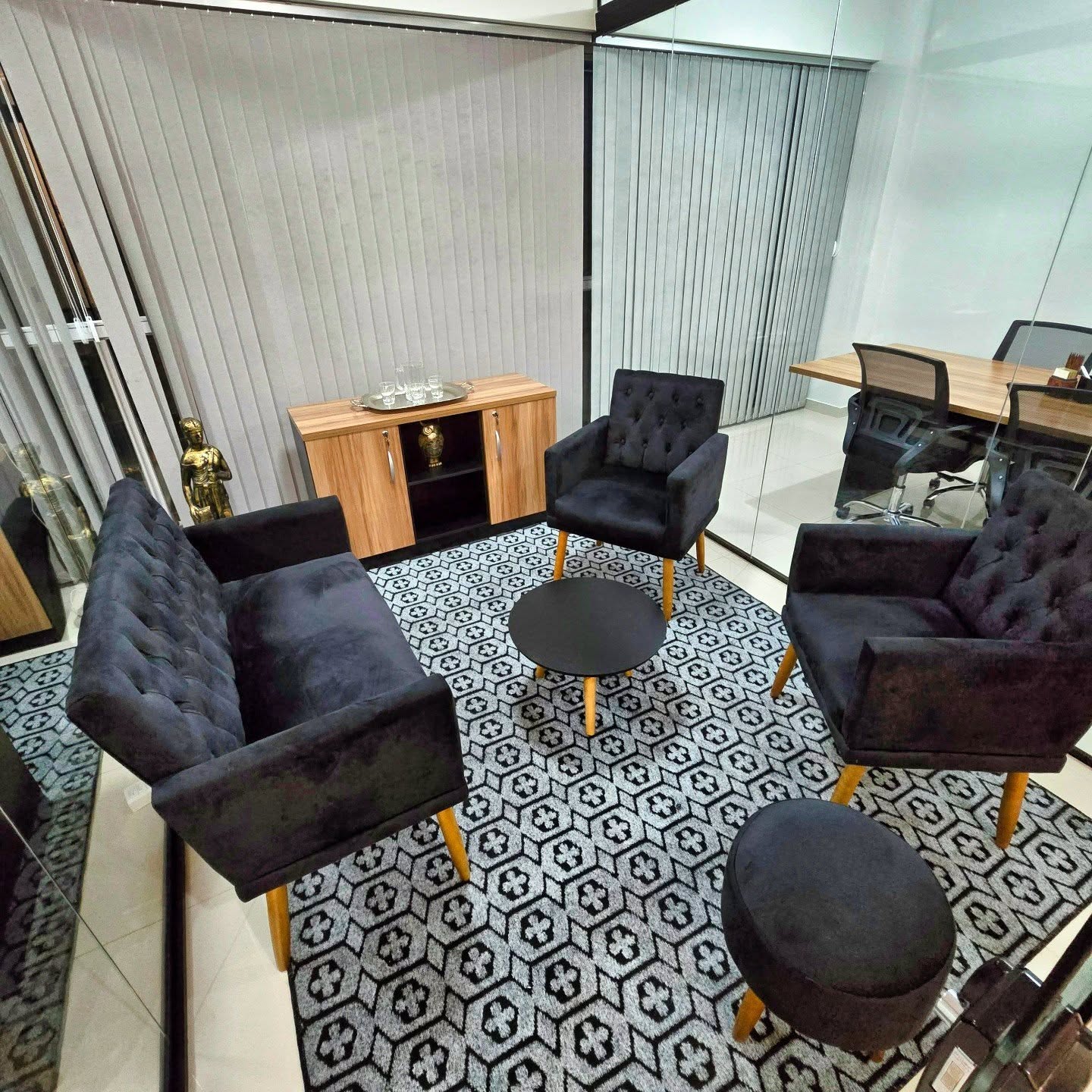 Sala de espera com sofá e poltronas pretas, mesa de centro redonda e tapete geométrico